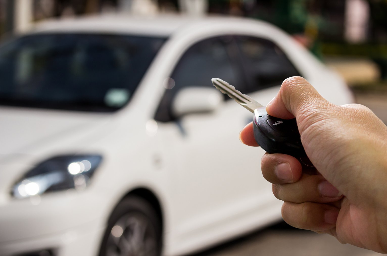 Female hand holding car key ready to start a new car with bl